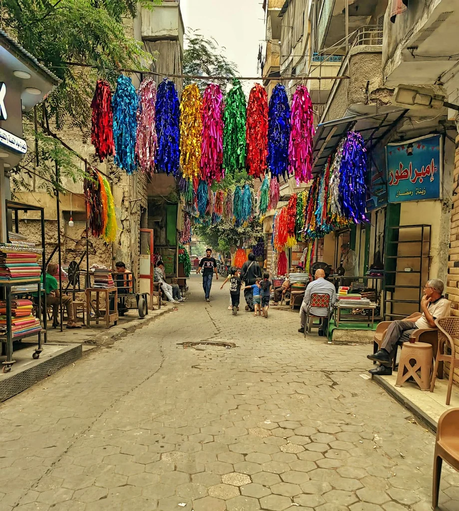 Colorful decorations hang over a bustling street market. - streamer